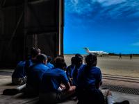 Students from Victor Scott Primary in Bermuda sit at the hangar door and look across the runway at one of the ACTIVATE aircraft.
