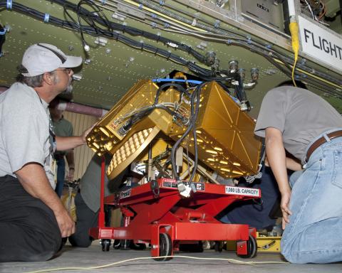 Technicians work on an instrument under a fuselage