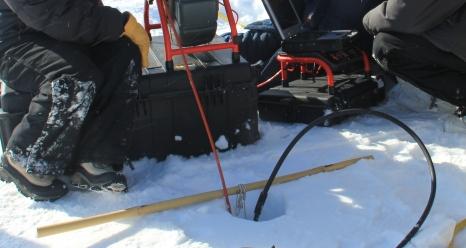 Glaciologist Lora Koenig (left) operates a video recorder that has been lowered into the bore hole to observe the ice structure of the aquifer in April 2013.