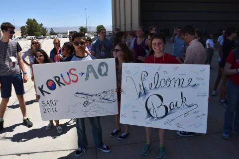 Kyle Kabasares (left), physics major at University of California Merced, and Mariah Heck (right), geophysics and geology major at University of Tulsa hold signs to welcome home the DC-8 crew home from the Korean U.S. Air Quality mission. Credits: NSERC Photo / Jane Peterson