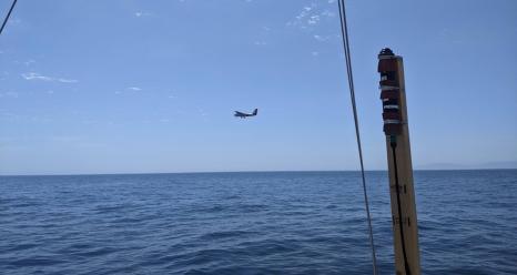 The Twin Otter research plane flies past RV Blissfully on sampling station. RV Blissfully’s surface light sensor is seen in the foreground. Photo by Bridget Seegers.