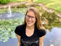 Just a picture of me. Long brown hair, glasses, black shirt. In front of a pond.